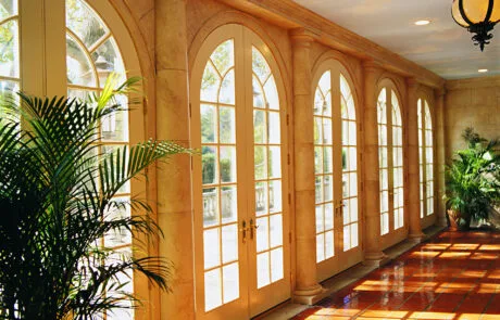 Arched wood doors along a sunlit hallway