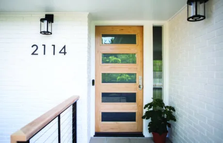Modern wood entry door with glass panels on a white brick home