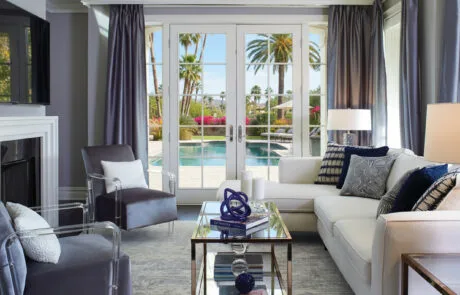 Living room with French doors opening to a pool and palm trees