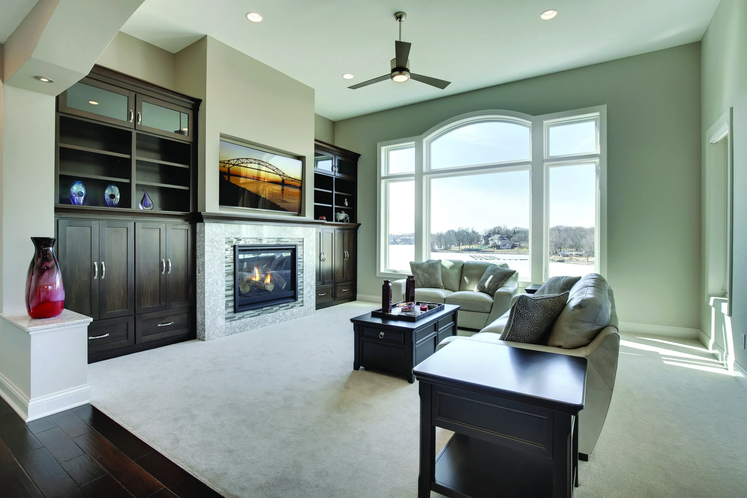 An arched window above a fireplace in a living room with built-in cabinetry