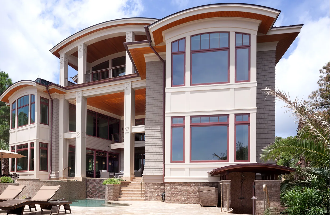 Three-story home with walls of framed windows rising above a pool terrace