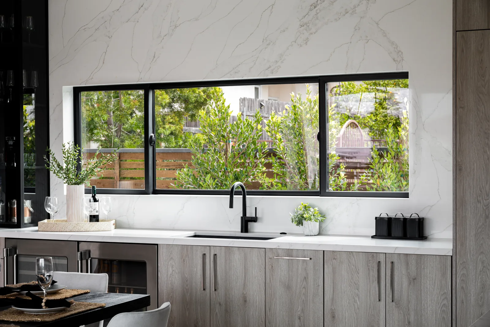 Wide black-framed window over a kitchen counter, looking out to planting