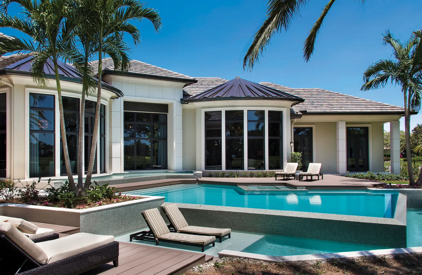 Single-story home with tall black-framed windows and a bay of glass behind a pool and palms