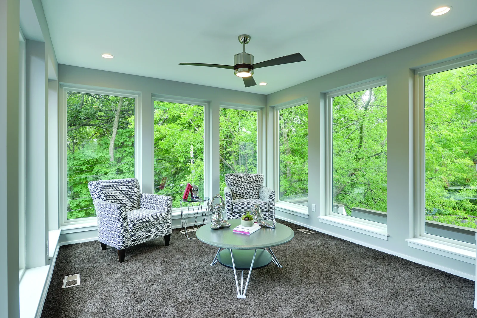 Sunroom wrapped in white-framed picture windows looking into trees