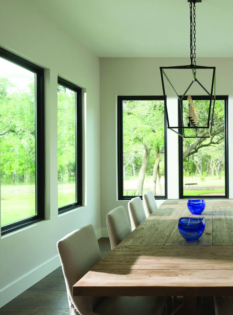 Dining room lit by tall black-framed windows looking out to green trees