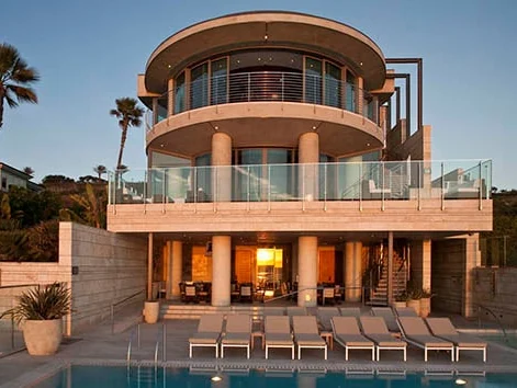 Curved sliding glass doors following the rounded face of a two-storey home above a pool terrace