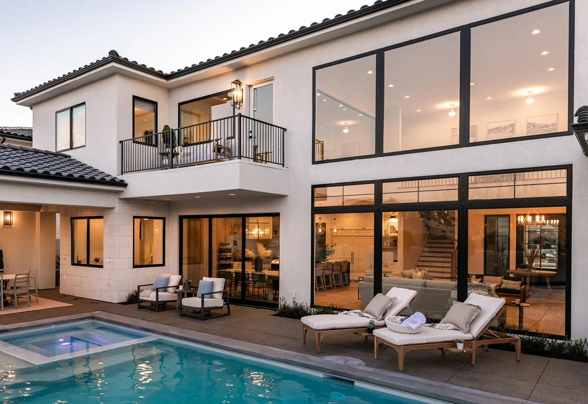 Two-storey stucco home with black-framed sliding glass doors opening onto a pool terrace