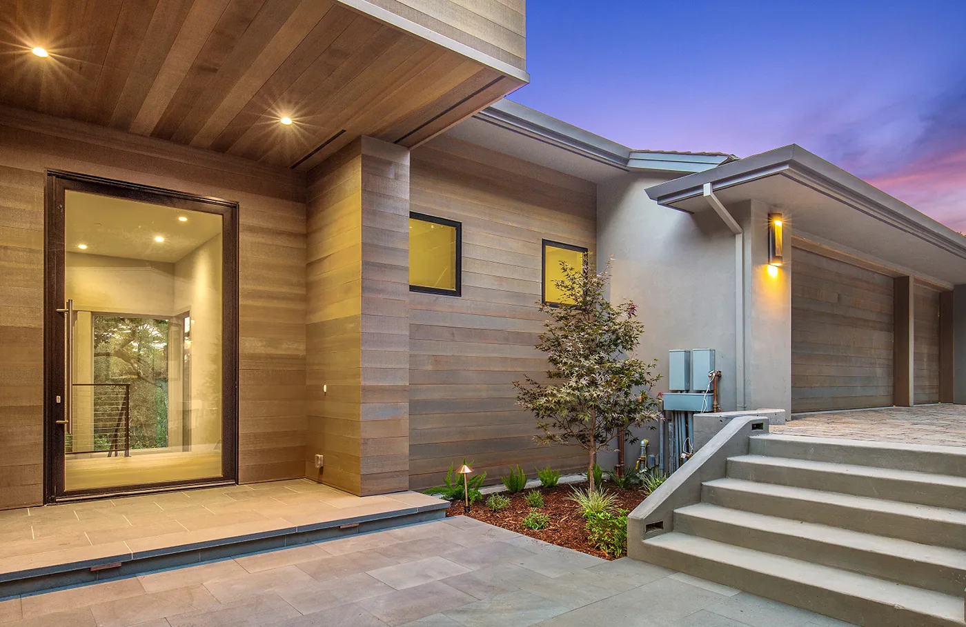 Tall glass entry door set into the wood-clad wall of a desert-modern home at dusk