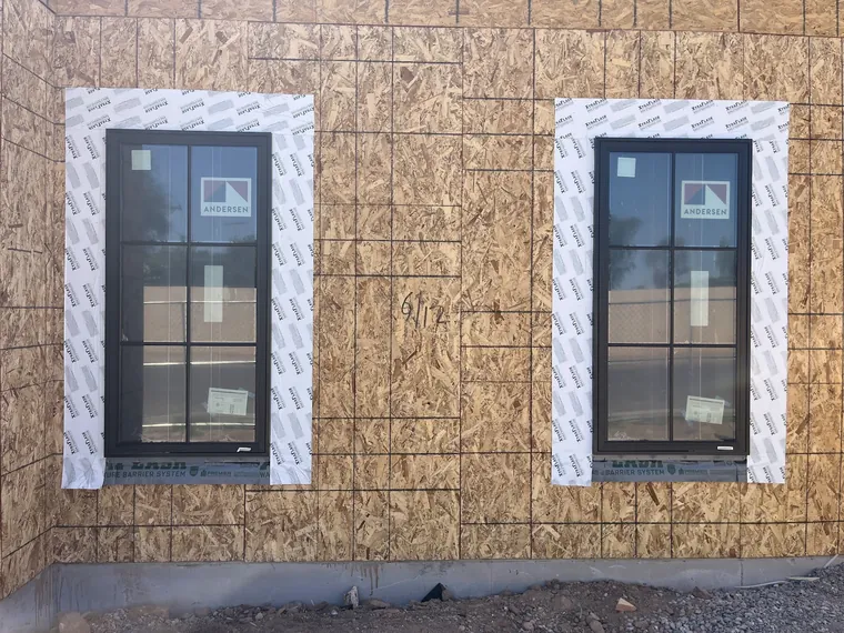 Two black framed new construction windows set into OSB sheathing with layout marks and flashing tape on a Phoenix build