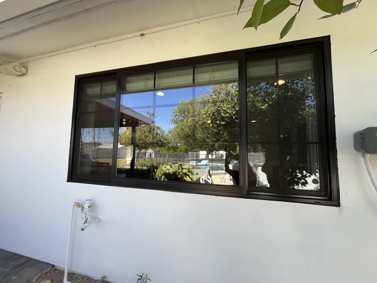 Wide black framed window on white stucco under a deep soffit on a finished Phoenix home