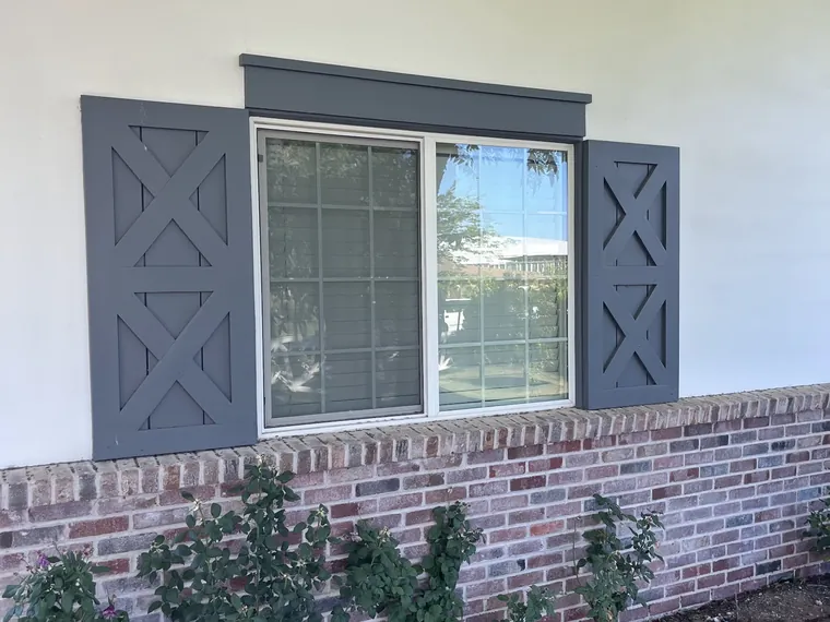 Black framed window with grey shutters over a brick wainscot on a finished Phoenix home