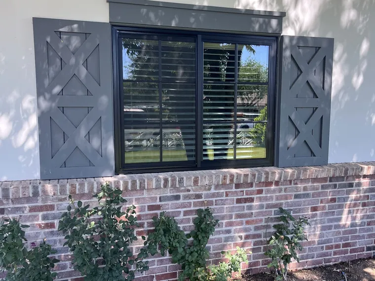 Black framed window with grey decorative shutters over a brick wainscot on a finished Phoenix home