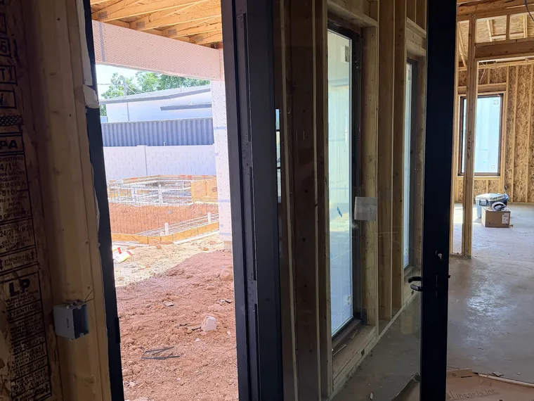 Black framed glass door standing open in a framed opening inside a Phoenix home under construction