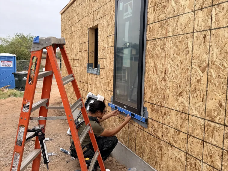 Noble installer levelling a black framed new construction window in a framed opening with a stepladder alongside