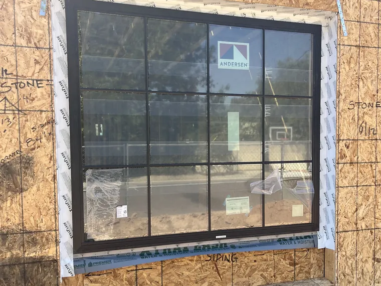 Large black framed picture window with a grille pattern set into a framed opening in the sheathing of a Phoenix new build