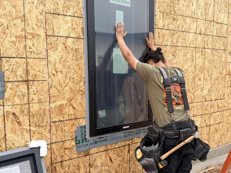 Noble installer holding a black framed new construction window into a framed opening in the sheathing