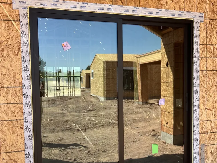 Black framed sliding glass door set into a framed opening in OSB sheathing on a Phoenix new build
