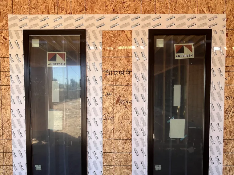 Two tall black framed new construction windows set into framed openings in OSB sheathing on a Phoenix build