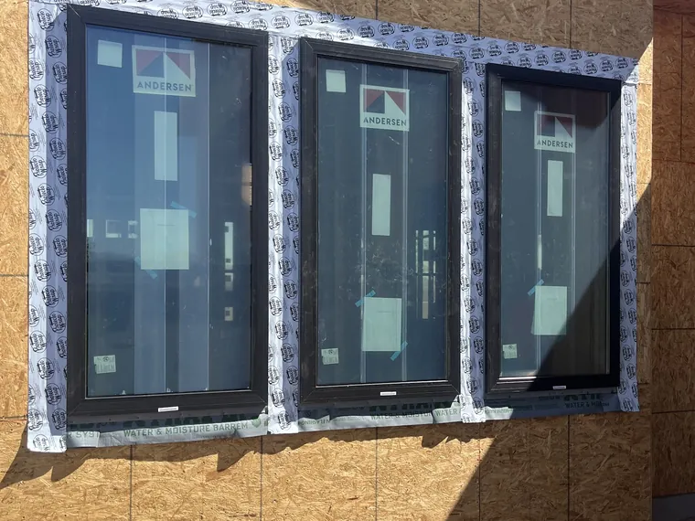 Three black framed new construction windows ganged into one framed opening in OSB sheathing on a Phoenix build