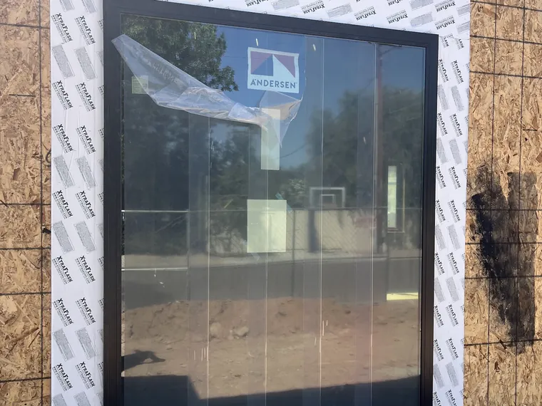 Wide black framed picture window set into a framed opening in the sheathing of a Phoenix new build