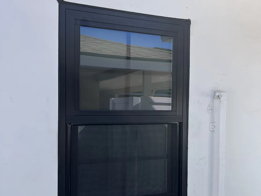 Black-framed single-hung replacement window in white stucco on a Noble project, the fixed upper sash above a lower sash that slides up