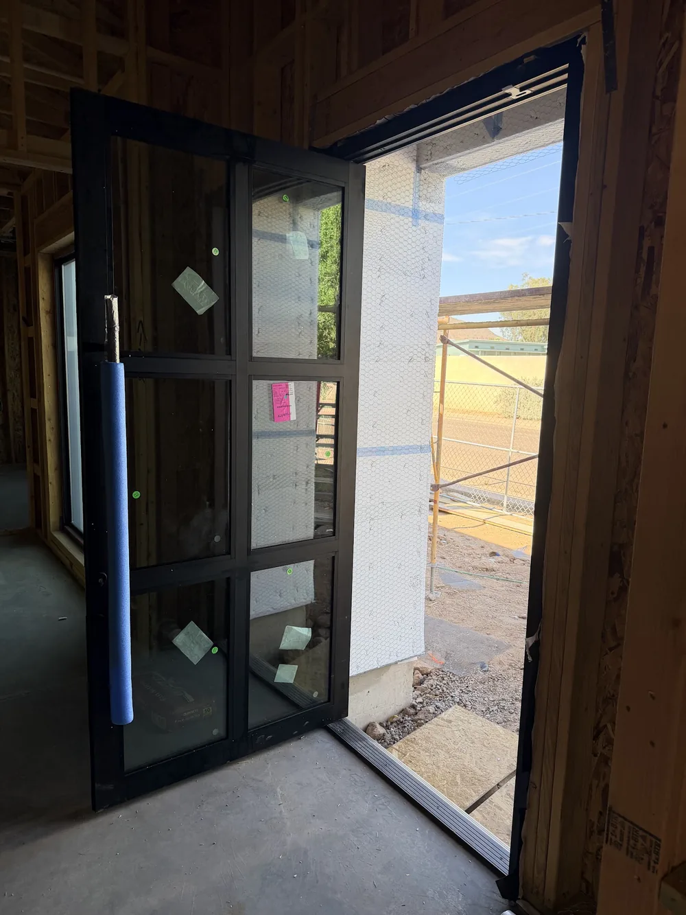 Tall black-framed glass entry door with a full-height pull, standing open on a Noble Windows & Doors project