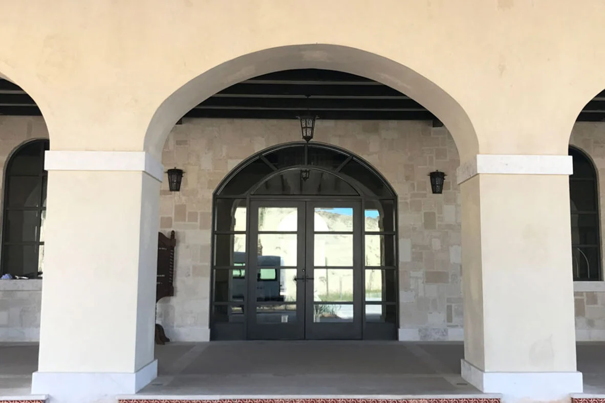 PRL Glass Systems aluminum double entry doors with an arched transom, set behind a stone loggia
