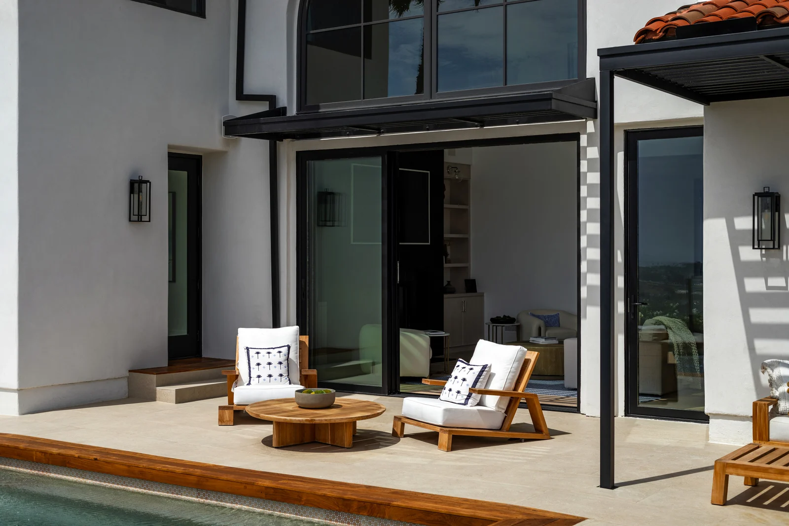 Sliding glass door panels stacked together at the left jamb of a stucco home, open onto a pool patio
